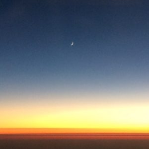 An endless horizon at sunset, with fingernail moon in sky